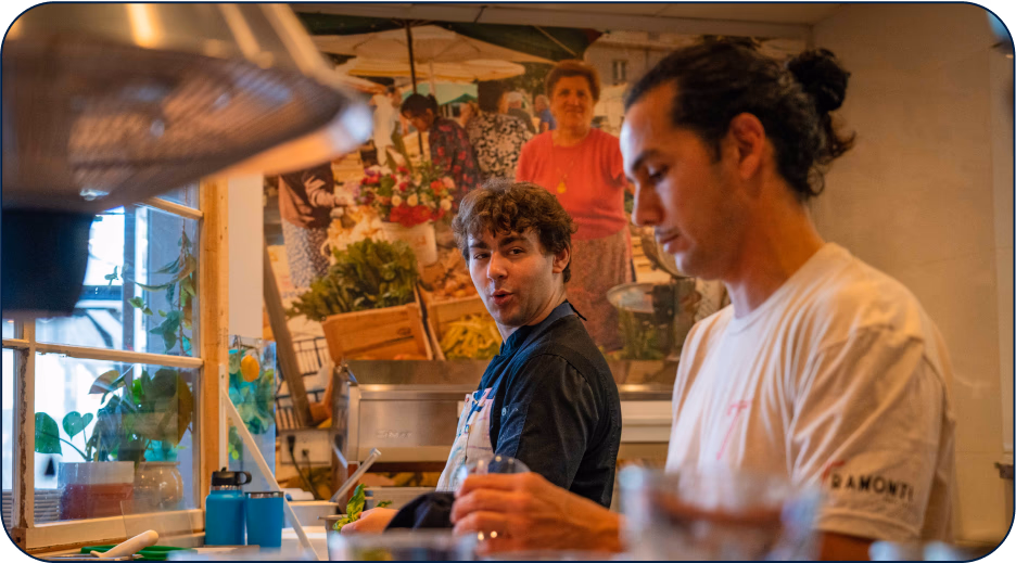 Two staff members working in a restaurant kitchen with a market mural on the wall